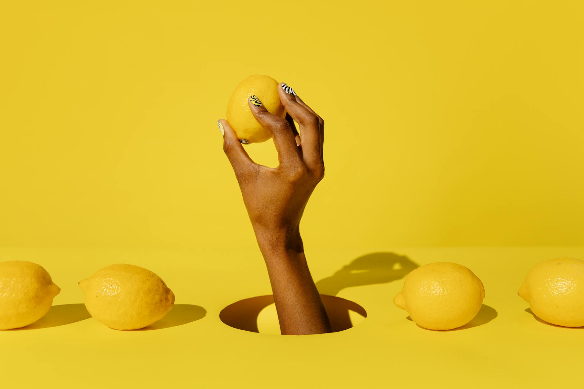 Hand holding a fresh lemon against a vibrant yellow background, symbolizing renewal and fresh sensation