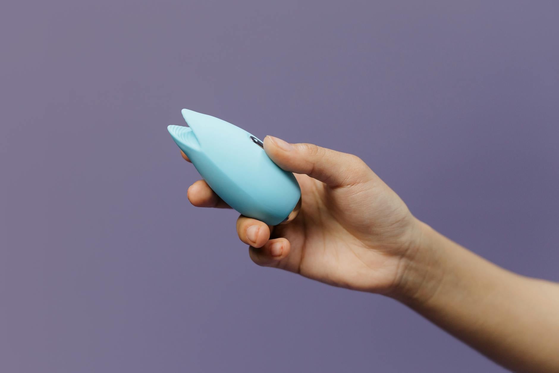 A soft silicone clitoral vibrator held in cupped hands, symbolizing gentle self-care and body reconnection during healing