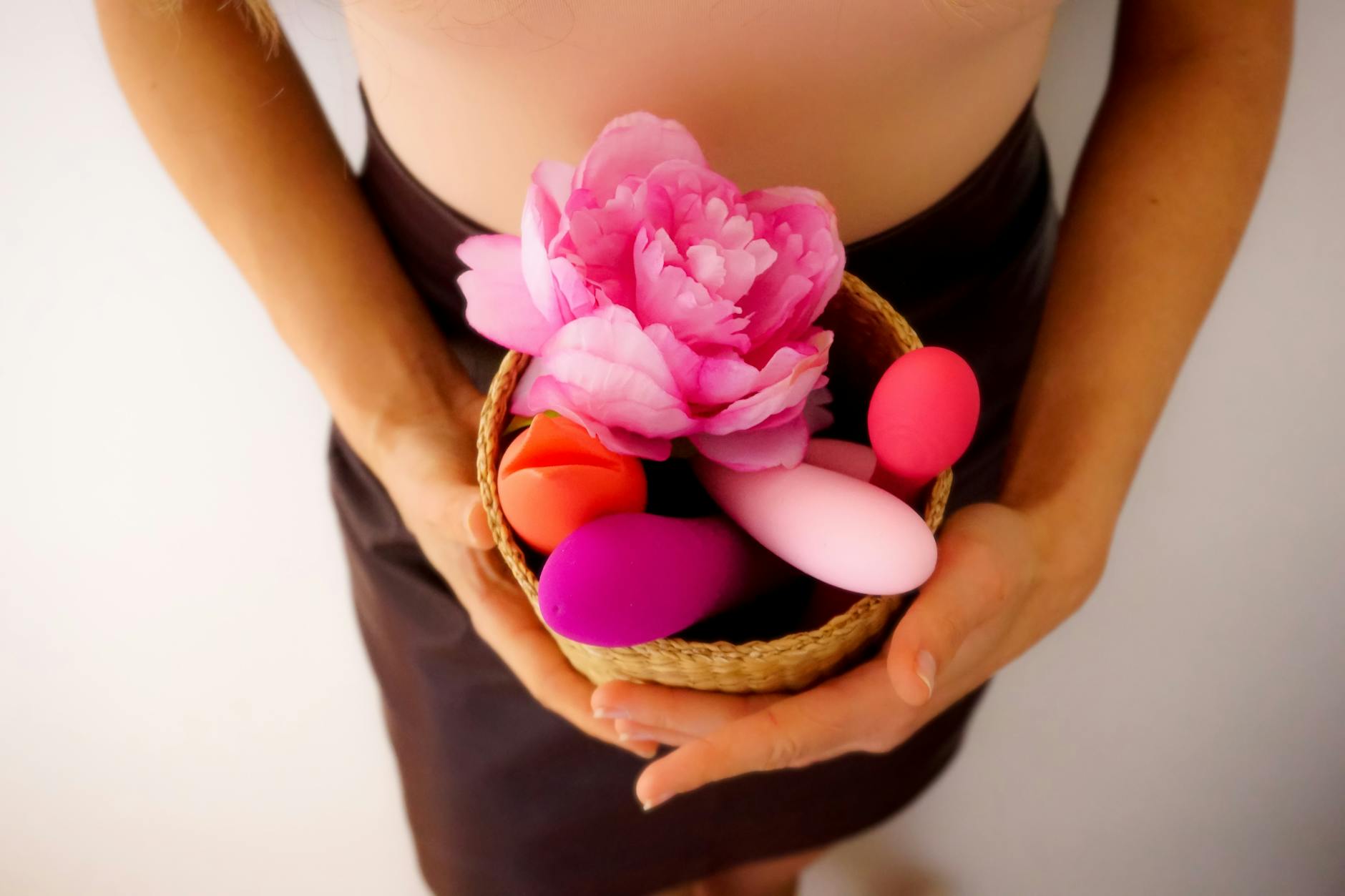 Colorful vibrators and intimate wellness tools in a basket with pink flowers